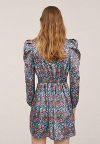 Blumenkleid mit puffärmel, tailliertem Schnitt und einem mehrfarbigen Muster aus Pink, Blau und Grün auf einem dunkleren Hintergrund.