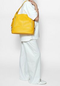 Geel lederen handtas met een gestructureerd ontwerp, voorzien van twee ritsvakjes en een enkele verstelbare schouderband.