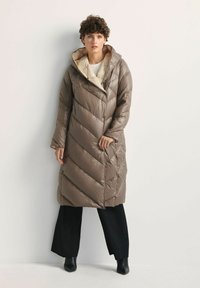 Długi, puszysty, brązowy pikowany płaszcz z kapturem, z ukośnym przeszyciem, ukrytym zapięciem na guziki i jasnym podszewką.