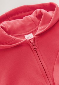 Koralfarvet hættetrøje med lynlås lavet af blødt stof, med en dobbeltsidet hætte, en lynlås i fuld længde og et mærke med teksten "NEXT".