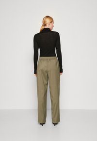 Schwarzes Langarmoberteil mit tailliertem Schnitt, kombiniert mit lockeren, olivgrünen Hosen mit elastischem Bund. Glatte Textur, minimalistischer Stil.