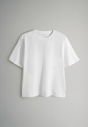 Vit t-shirt med korta ärmar visas mot en ljus bakgrund. Tillverkad av slät tyg, med rund halsringning och rak silhuett.