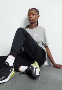 Nike grå t-shirt med hvidt logo, sorte sweatpants med lommer og sorte sneakers med grønne detaljer og hvide såler. Glatte teksturer.