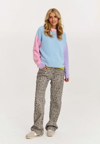 Sweter w kolorze bloków w pastelowym niebieskim i różowym z długimi rękawami, w połączeniu z spodniami w leopardzi wzór i beżowymi sneakersami.