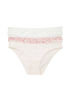 Jeune femme portant un t-shirt blanc uni à manches courtes et un sous-vêtement beige clair taille haute, debout sur un fond blanc.