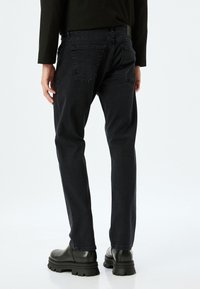 Jeans de mezclilla negra con un diseño de pierna recta. Presentan dos bolsillos traseros, costuras minimalistas y un acabado texturizado. Llevados con botas negras.