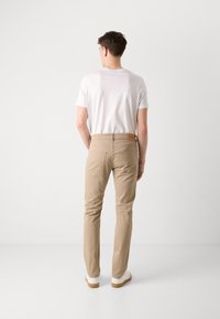 Beige katoenen broek met een strakke pasvorm, achterzakken en een leren logo-label op de tailleband, gecombineerd met een effen wit T-shirt.