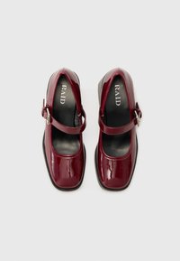Burgundy patent leather Mary Jane shoes with a round toe, ankle strap, and black rubber sole, featuring a smooth, glossy texture.