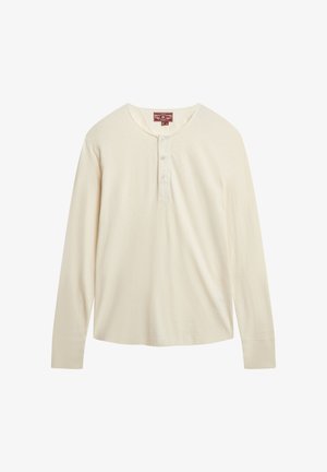 Chemise à manches longues de style henley en tissu couleur crème avec une texture douce, dotée d'une patte de boutonnage à trois boutons et d'un ourlet incurvé.