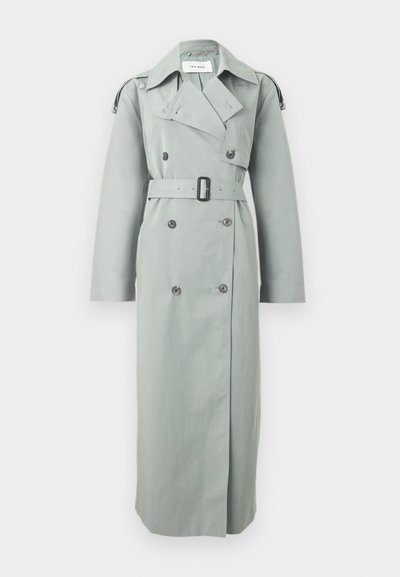 Μακρύ γκρι διπλόμπουτο παλτό τύπου τρανς με φαρδιές πέτες, μαύρη αγκράφα ζώνης, λεπτομέρειες με κουμπιά και επιγονατίδες στα μανίκια.