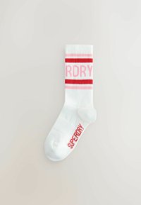 Biała bawełniana skarpeta z czerwonymi paskami i tekstem "SUPERDRY" napisanym dużymi literami, o miękkiej fakturze i długości do kostki.