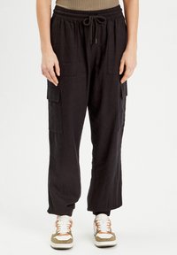 Pantalons cargo en lin noir avec une taille élastique, fermeture à cordon, deux poches latérales et une coupe fuselée au niveau des chevilles.