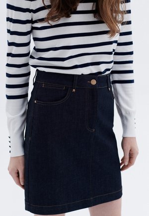 Denim rok in donkerblauw met zichtbare stiksels, een sluiting met knopen aan de voorkant en zijzakken. Gecombineerd met een wit en marineblauw gestreept sweater.
