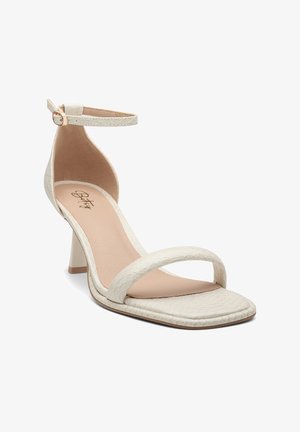 White heeled sandals featuring a textured snake print design, open toe, and ankle strap with a small gold buckle. Square-shaped heel.
