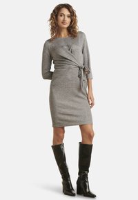 Gray wrap dress with three-quarter sleeves, textured fabric, fitted silhouette, tied waistband, paired with knee-high black heeled boots.