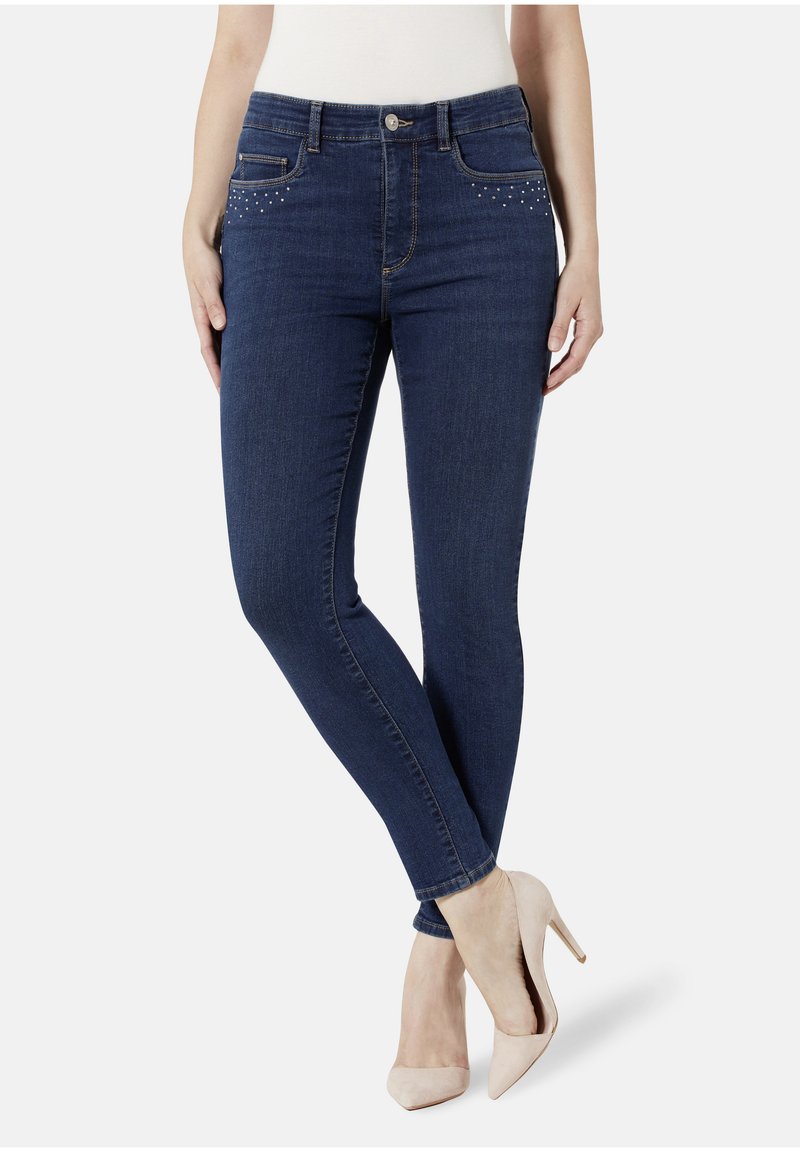 Dunkelblaue Jeans im Skinny-Fit-Stil haben eine mittelhohe Taille, vordere Taschen mit dekorativen Nietenakzenten und eine taillierte Silhouette.