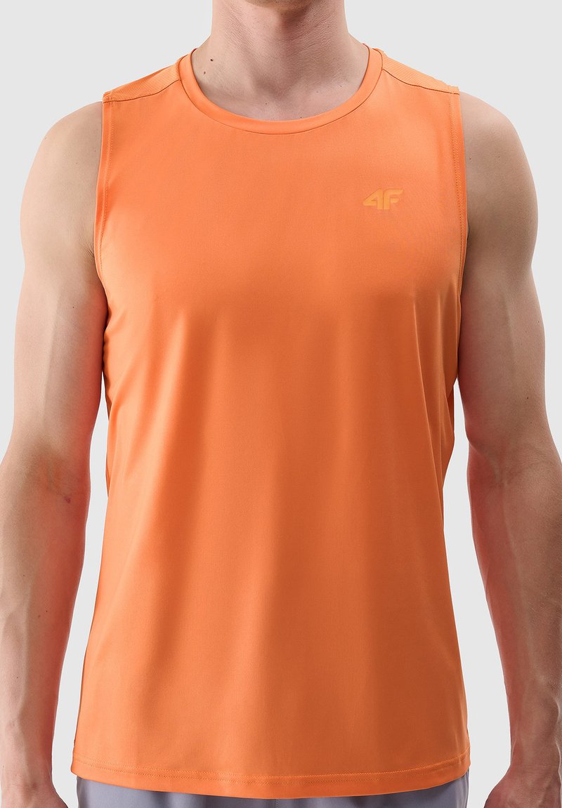 Homme portant un débardeur de sport orange sans manches avec un petit logo sur la poitrine, debout devant un fond clair uni.