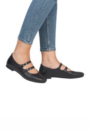 Schwarze Leder-Mary-Jane-Schuhe mit zwei vorderen Riemen und runden Schnallen, spitzer Zehenform und flacher Sohle. Getragen mit verkürzten blauen Jeans.