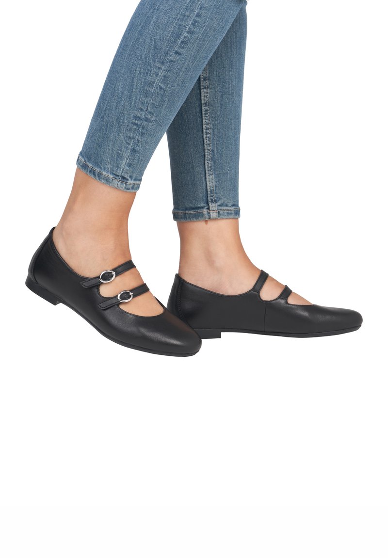 Schwarze Leder-Mary-Jane-Schuhe mit zwei vorderen Riemen und runden Schnallen, spitzer Zehenform und flacher Sohle. Getragen mit verkürzten blauen Jeans.