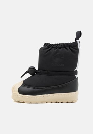 Botte d’hiver isolée noire et beige avec cordon élastique et verrou, bout en caoutchouc et logo Adidas sur la partie supérieure rembourrée.