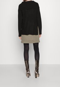 Svart oversized tröja med ribbad krage, kombinerad med en beige kjol. Modellen bär svarta strumpbyxor och blanka knähöga silverskor.