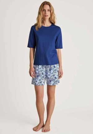 Blauwe katoenen T-shirt met korte mouwen, gecombineerd met witte shorts met een blauw bloemenpatroon. De outfit is casual en heeft een ontspannen pasvorm.