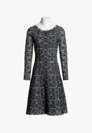Robe en dentelle noire avec manches longues et motif floral, corsage ajusté et jupe évasée présentée sur un buste de mannequin blanc.