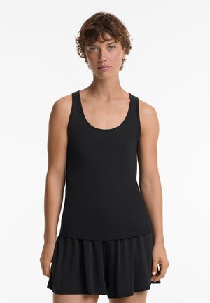 Schwarzes Tanktop mit Rundhalsausschnitt, aus glattem Stoff gefertigt. Kombiniert mit einem locker sitzenden schwarzen Rock mit ausgestelltem Saum.