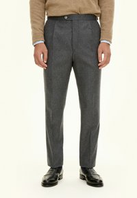 Grå ullbyxor med en skräddarsydd design, med framfall och knappstängning. Bärs med en beige tröja och svarta skor.