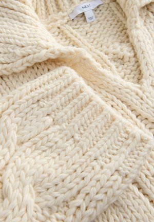 Cárdigan de punto en color crema con hilo grueso, textura acanalada y cuello chal. La etiqueta indica la marca "NEXT".