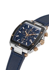 Orologio quadrato con quadrante in blu navy texture, dettagli in oro rosa, cassa in acciaio inossidabile e cinturino in pelle blu. Presenta tre sotto-quadranti e display della data.