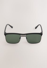 Occhiali da sole rettangolari neri con lenti verde scuro, dettagli in metallo e aste nere sottili. Presentano un design elegante e minimalista.