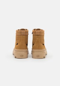 Bottes Chelsea en daim beige avec un col replié, semelle en caoutchouc et logo embossé à l'arrière. Présente des languettes pour un enfilage facile.
