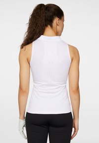 Vit ärmlös polo med krage, med en texturerad baksida med perforeringar och vertikala sömdetaljer. Matchad med svarta byxor.