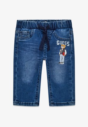 Niebieskie dżinsy dla malucha z elastycznym pasem, sznurkiem i bocznymi kieszeniami, z grafiką misia i napisem "GUESS" na prawej nogawce.