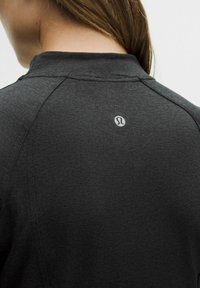 Dunkelgraues Langarmshirt mit hohem Kragen. Weiche Stoffstruktur und Raglanärmel. Auf der Rückseite befindet sich ein kleines weißes Logo.