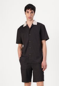 Ensemble de chemise à manches courtes et de shorts noir avec des rayures verticales, col crème contrastant, bouton sur le devant et coupe décontractée.