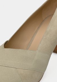 Chaussure à talon haut beige avec un corps en daim lisse, des accents de bande élastique et une forme d'orteil arrondie avec un talon imitation bois.