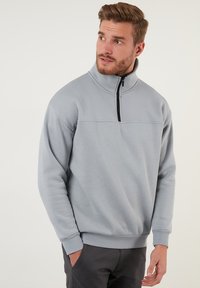 Sudadera de color gris claro con medio cierre en el cuello, puños acanalados y un diseño de yugo de costura plana. Textura de tela suave.