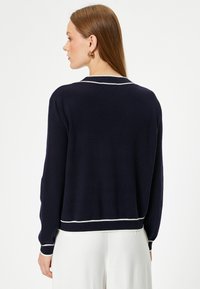 Mörkblå tröja med vit kant, ribbade ärmslut och nederkant, mjuk textur, klassisk silhuett och design med rund hals, som visar upp en minimalistisk stil.