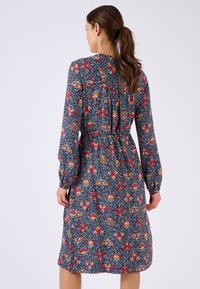 Abito a maniche lunghe in blu navy con un motivo floreale in rosso, giallo e bianco. Presenta un punto vita arricciato e una chiusura a chiave sul retro.