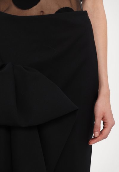 Black skirt featuring a large bow detail at the front, made of a smooth fabric with a structured shape. The design is sleek and minimalist.