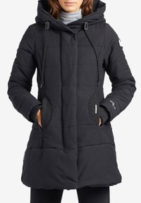 Svart quiltad pufferjacka med huva, snörningsstängning, sidofickor och ribbade ärmslut. Har en slät yta och minimalistisk design.