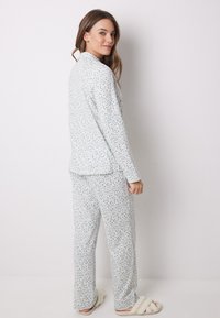 Ljust blå pyjamasset i mjukt tyg, med ett prickigt mönster. Skjortan har krage och byxorna är löst sittande. Mjuka tofflor fulländar looken.