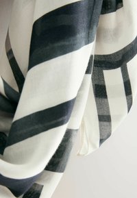 Sciarpa bianca e nera con audaci motivi a strisce, realizzata in un tessuto leggero e trasparente con una texture morbida e una caduta fluida.