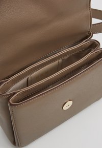 Sac à main marron DKNY avec finition texturée, comprenant plusieurs poches intérieures et un accent de ferrure dorée sur le devant.