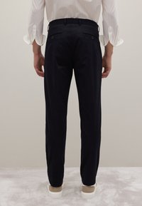 Marineblauwe broek gemaakt van een gladde stof, met twee achterzakken met knopen en een slim fit, gecombineerd met lichtgekleurde sneakers.