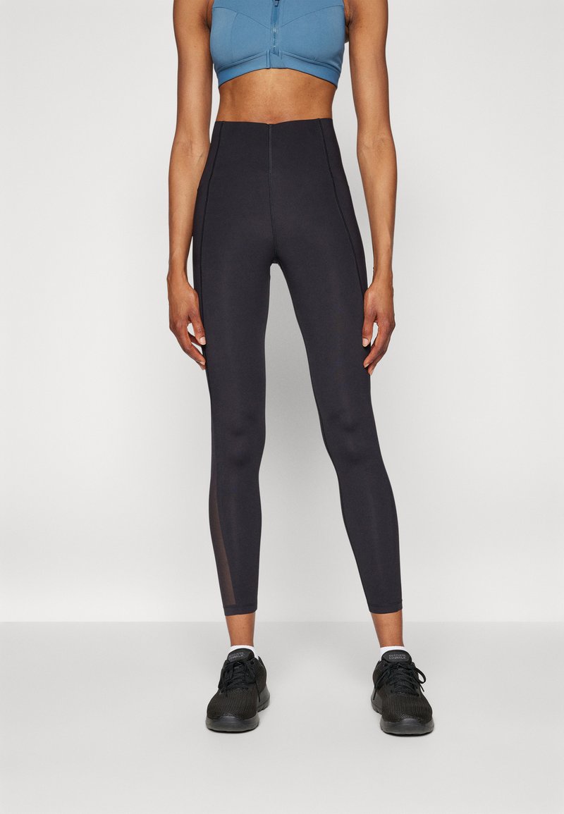 High-waisted black leggings with a smooth texture, featuring mesh panels on the lower legs. Paired with a blue cropped sports top and black sneakers.