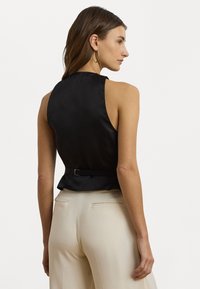Černý saténový top s vysokým výstřihem, bez rukávů a s peplum detailem, se páskem kolem pasu.