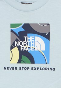 Το λογότυπο της The North Face με αφηρημένο πολύχρωμο φόντο και το κείμενο «Ποτέ μην σταματάς να εξερευνάς» από κάτω σε ανοιχτό ύφασμα.